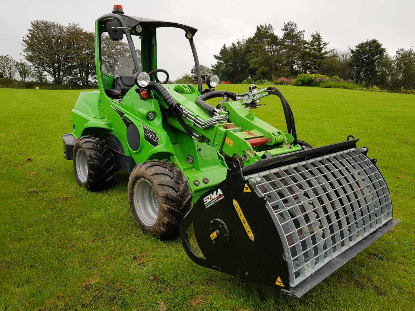 Green mini loader with attachment on grass field