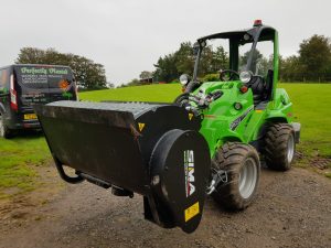 Green tractor with front attachment on grassy field.