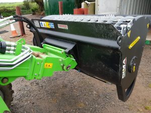 Green agricultural machine attachment on farm dirt ground.