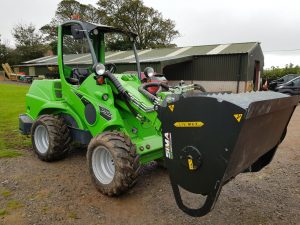 Green loader with bucket outside barn