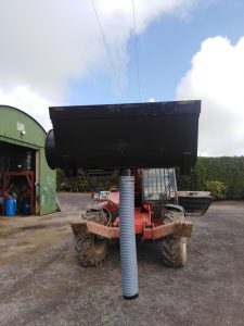 Tractor with large attachment in a farmyard.