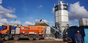 Concrete mixer truck beside silo in construction site.