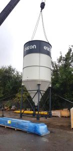 Crane lifting large industrial silo in yard.