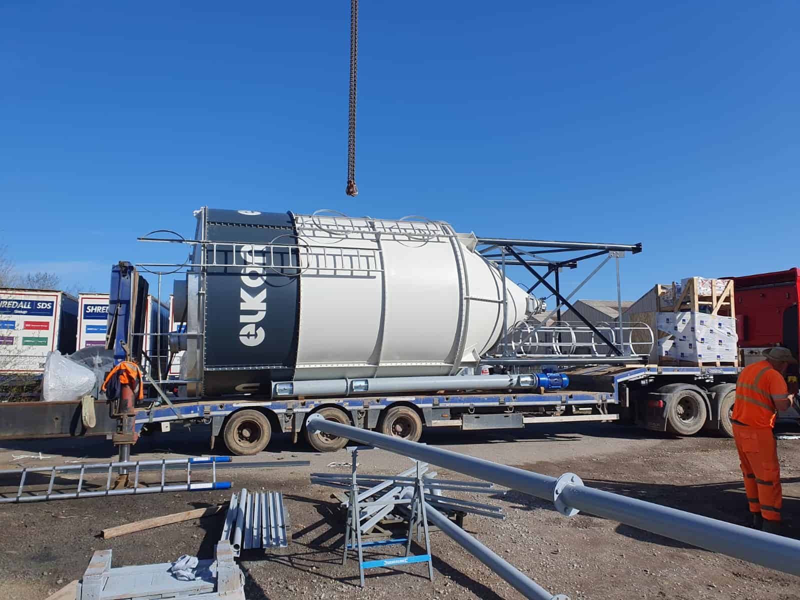 Construction workers handling large silo on lorry.