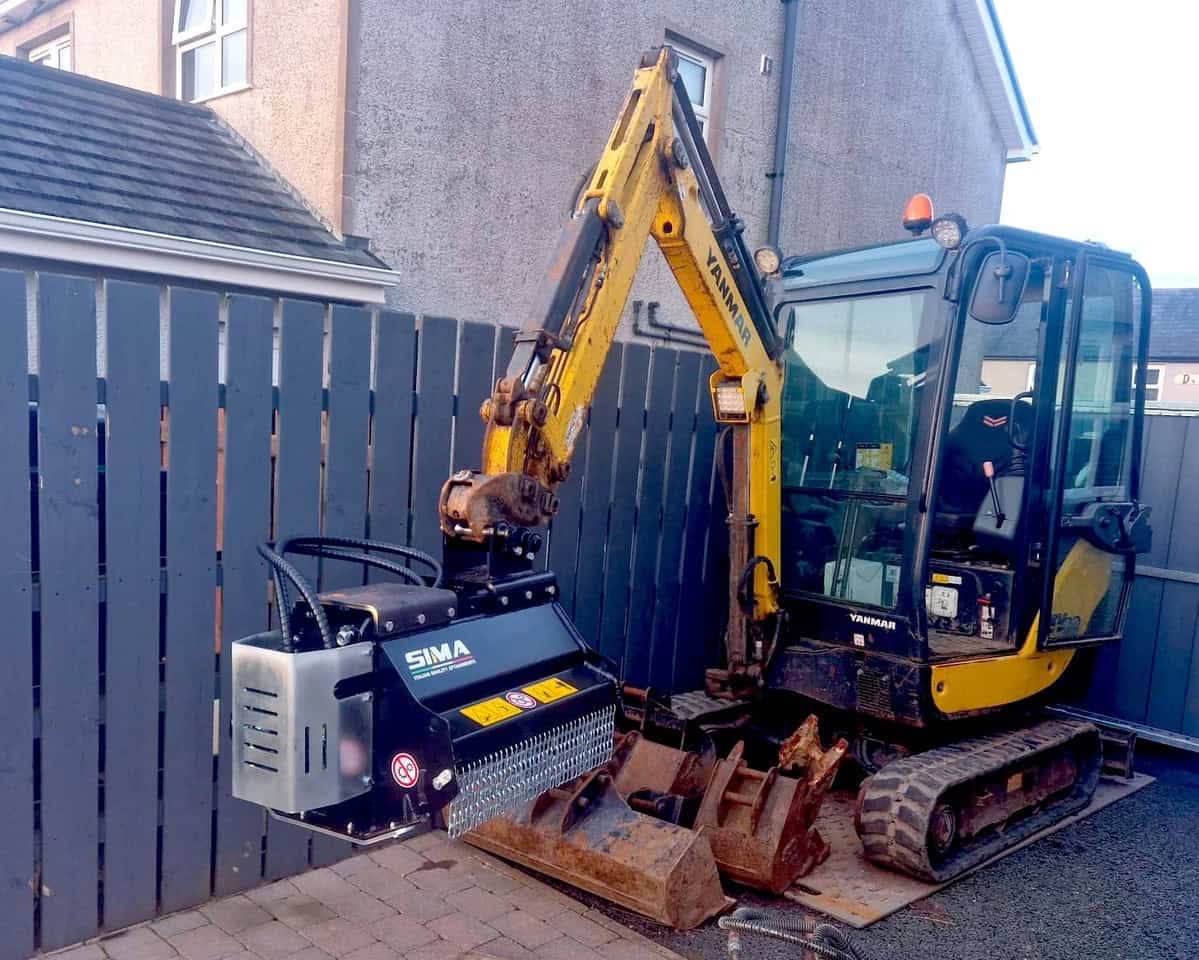 Mini digger with attachment next to fence.